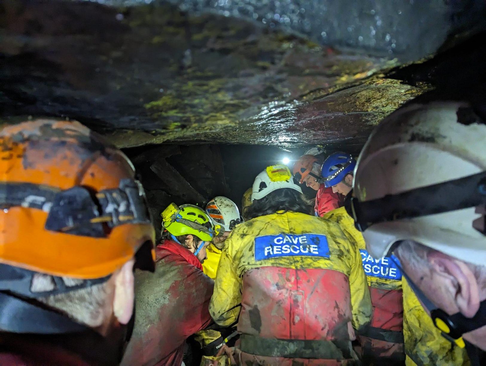 SCRO team members in cave rescue suits working in a low underground passage